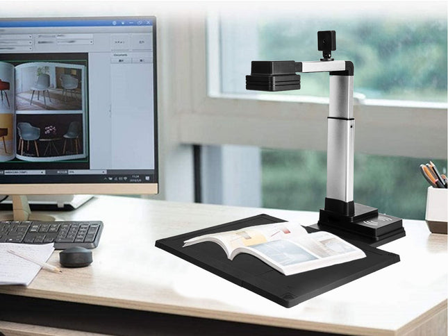 Book being scanned by a document camera on a desk with a computer monitor in the background.