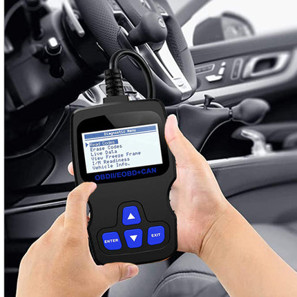 A handheld black OBD2 diagnostic scanner with blue buttons and a screen showing menu options, held by two hands in front of a car dashboard and steering wheel.