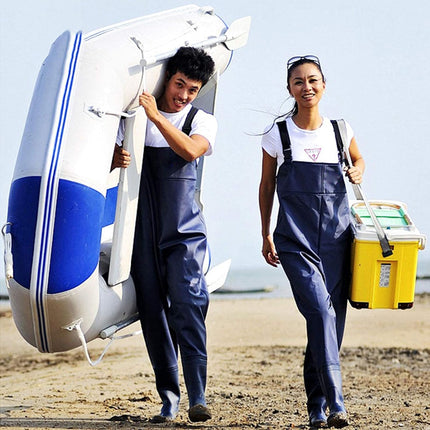 Two people in overalls walking on a beach with a small boat and cooler.