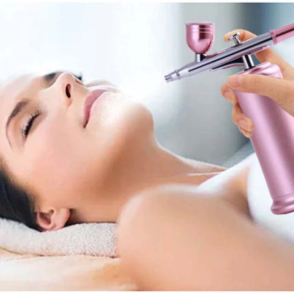 A close-up lifestyle shot of a woman receiving a facial spray treatment, lying on a spa bed with her eyes closed while a hand holds a pink and silver spray bottle near her face.