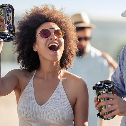 A woman with an afro hairstyle and pink-tinted sunglasses holds up a colorful beverage can with a straw hat and sunglasses in her other hand, smiling at a sunny outdoor party.