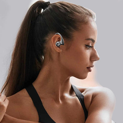 A woman in a black sports bra wearing a black and silver wireless earbud, shown in profile against a neutral gray background.