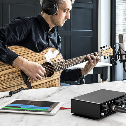 Man playing a guitar with a device on a table, possibly recording or monitoring audio.