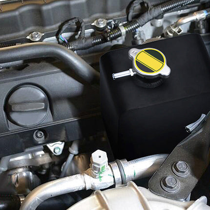 A black engine cover or protective wrap fitted over a translucent plastic reservoir with a yellow and black cap, installed in a car engine bay.