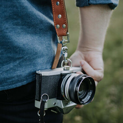 Person holding a vintage camera with a leather strap against a blurred natural background