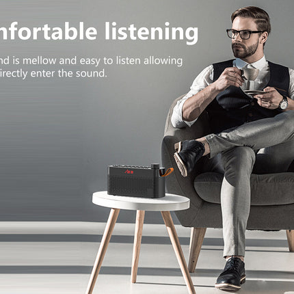 A man in a gray armchair wearing glasses, a white shirt, and a black vest sits beside a small white table holding a black portable speaker. The scene is set against a gray wall with text on the left reading 'Comfortable listening'.