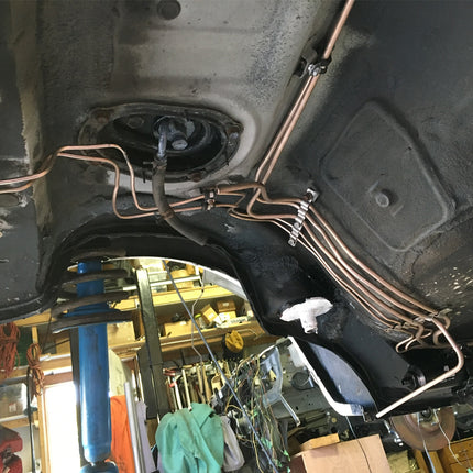Undercarriage of a vehicle with visible wiring and mechanical components in a workshop setting.