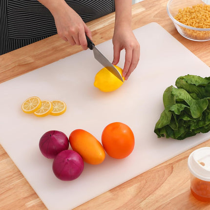 Person cutting a lemon on a white cutting board with vegetables and a bottle of oil.