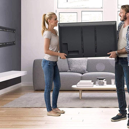 Man and woman holding a large flat-screen TV in a living room.