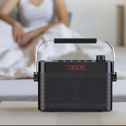 Black portable radio with digital display on a surface, with a blurred person in bed in the background.