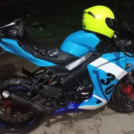 A blue, white, and black sport motorcycle parked outdoors at night, with a bright yellow helmet resting on the seat area.