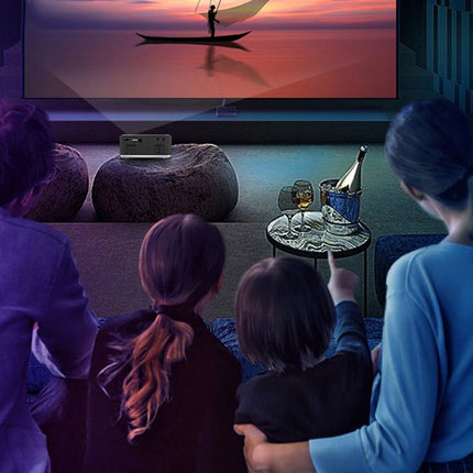 People watching a sunset over water scene projected onto a screen in a dimly lit room.