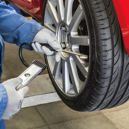 Person changing a tire on a red car using a tool.