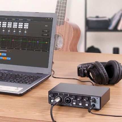 Laptop with audio software, guitar, headphones, and audio interface on a desk.