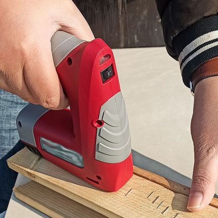 A red and gray cordless nail gun being used outdoors to fasten a piece of wood, with a person's hands guiding it along the board.