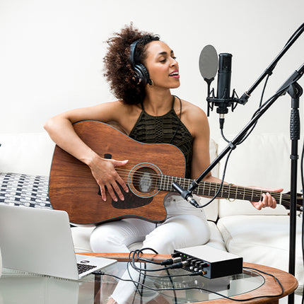 Woman playing guitar and singing into a microphone in a home studio setting.