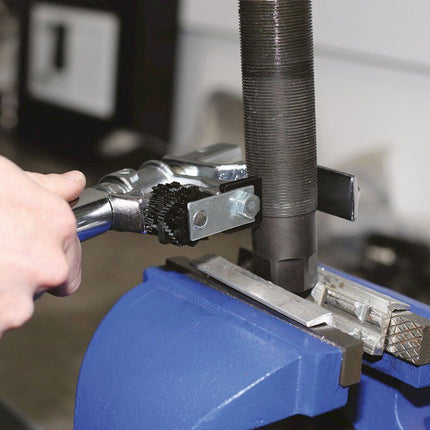 Person using a tool on a metal object held in a blue vise.