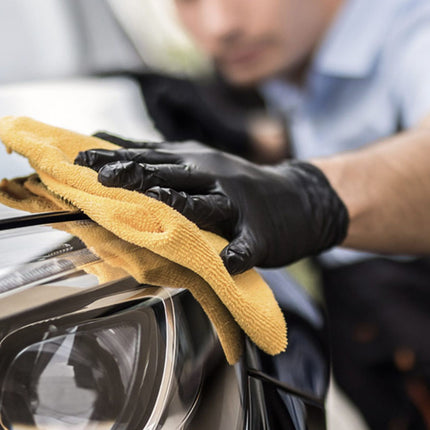 Person cleaning a car with a yellow microfiber cloth and black gloves