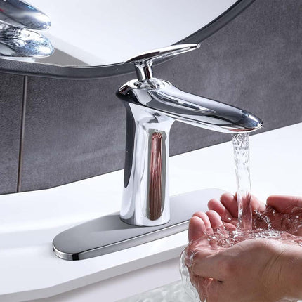 A polished chrome single-handle bathroom faucet with water running from the spout, shown installed on a white sink with a person's hands cupping the water. A round mirror is visible in the background.