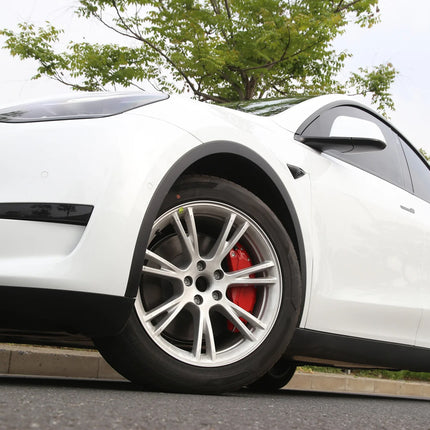 White car with red brake caliper on a road with trees in the background