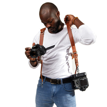 Man holding a camera with a strap, wearing a white shirt and blue jeans on a white background