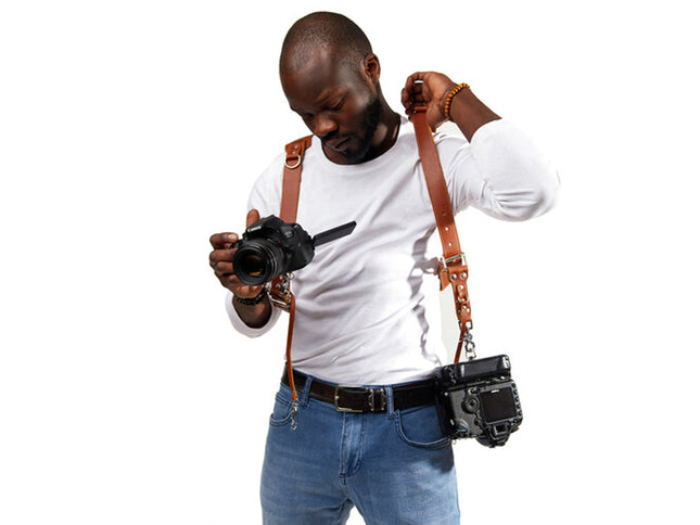 Man holding a camera with a strap, wearing a white shirt and blue jeans on a white background