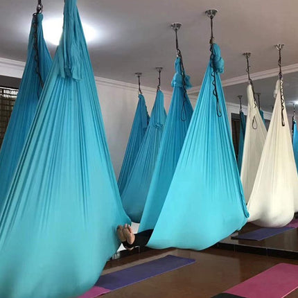 Yoga hammocks hanging from the ceiling in a room with yoga mats on the floor.