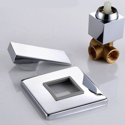 A polished chrome shower valve trim set on a light gray reflective surface, including a square faceplate with a recessed center, a matching rectangular cover piece, and a brass shower valve with a chrome top cap.