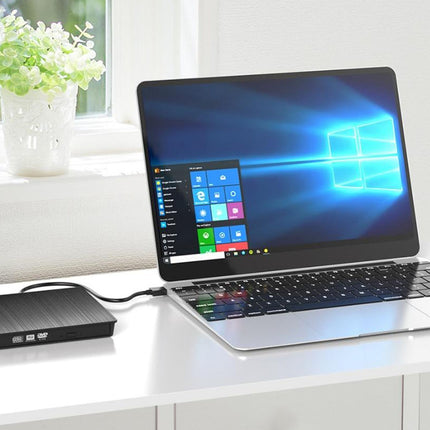 Laptop with Windows operating system on screen, connected to a external hard drive on a white desk.