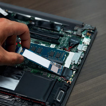 Person installing an SSD into a laptop's open motherboard