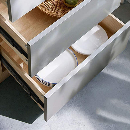 Open drawer of a kitchen cabinet with white plates inside on a gray floor.