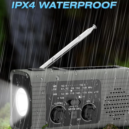 A gray portable emergency radio with a silver telescoping antenna, shown outdoors in the rain with water droplets on its surface. The radio has a built-in flashlight on the front left, a speaker grille on the right, and control knobs.