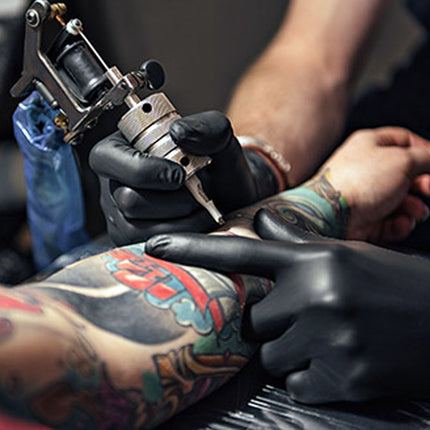 Tattoo artist at work with a tattoo machine on a client's arm.