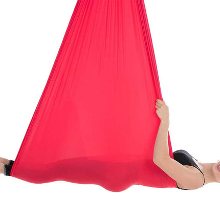 Person lying on a red aerial yoga hammock against a white background