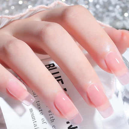 A close-up of a hand with long, glossy French-tip press-on nails in a soft pink and white ombre style, resting over a clear glass bottle with printed text.