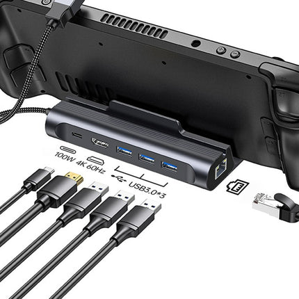 A black gaming controller dock and hub device shown with a game controller attached, plus several cables and port labels on a white background.