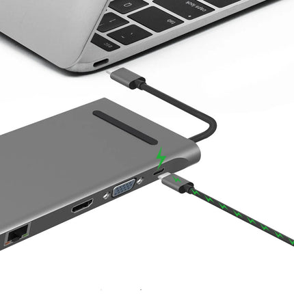 A gray portable hub or dock connected to a silver laptop, with a black and green cable plugged into one of its ports on a white background.