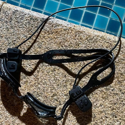 Black swim goggles on a concrete ledge with a pool in the background