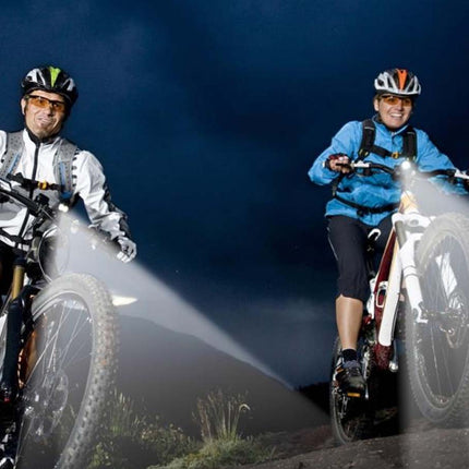 Two cyclists on mountain bikes with headlamps against a dark sky.