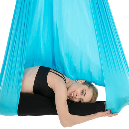 Woman lying in a blue aerial yoga hammock against a white background