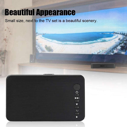 Black electronic device with buttons displayed in front of a TV showing a beach scene.