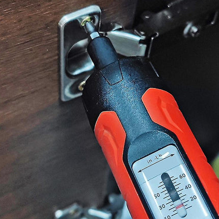 A close-up of a red and black handheld screw tension meter being used to tighten a screw on a metal cabinet hinge against a dark wood surface.