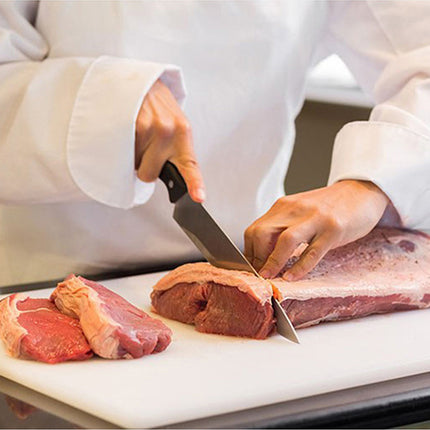Person in a white coat cutting raw meat on a white cutting board.