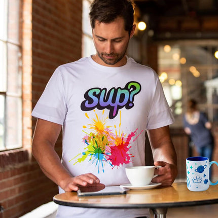 Man wearing a white t-shirt with colorful text and design, sitting at a table with a coffee cup and smartphone.