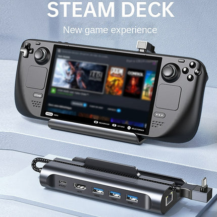 Steam Deck handheld gaming console shown with its attached power adapter and multiple USB ports, displayed on a clean light blue studio background with the text 'STEAM DECK' and 'New game experience' at the top.