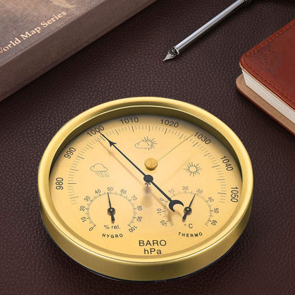 Gold barometer on a dark surface with a book and pen in the background