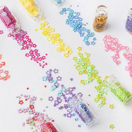Clear plastic bottles filled with colorful star-shaped glitter flakes, with the bottles tipped so the glitter spills out in rainbow-colored streams on a white background.