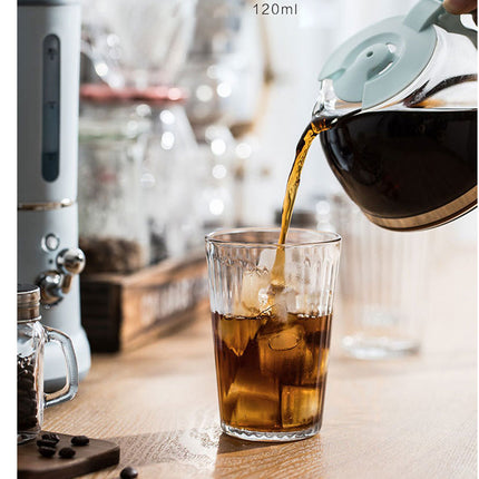 A clear glass 120ml iced coffee glass on a wooden table, with coffee being poured from a glass kettle into it.
