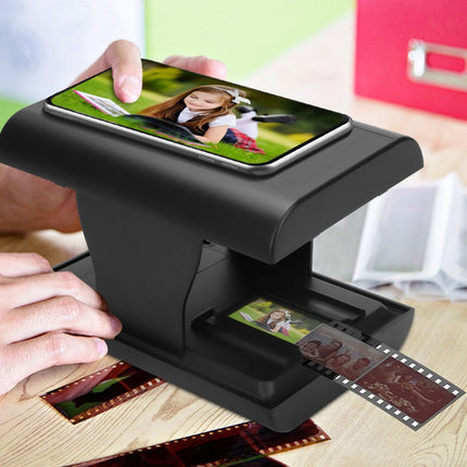 Film scanner with smartphone displaying a photo, scanning old film negatives on a wooden table.
