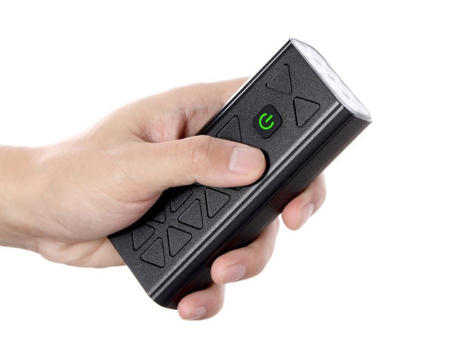 Hand holding a black electronic device with a green power indicator on a white background